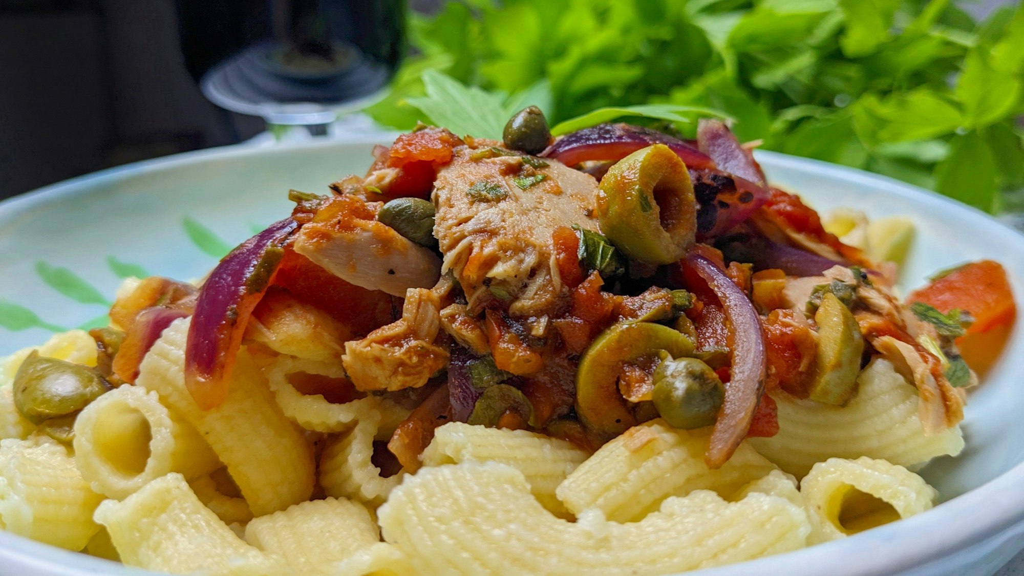 Auf Röhrennudeln ist die Soße aus Zwiebeln, Oliven, Kapern, Thunfisch und Maggikraut zu sehen.