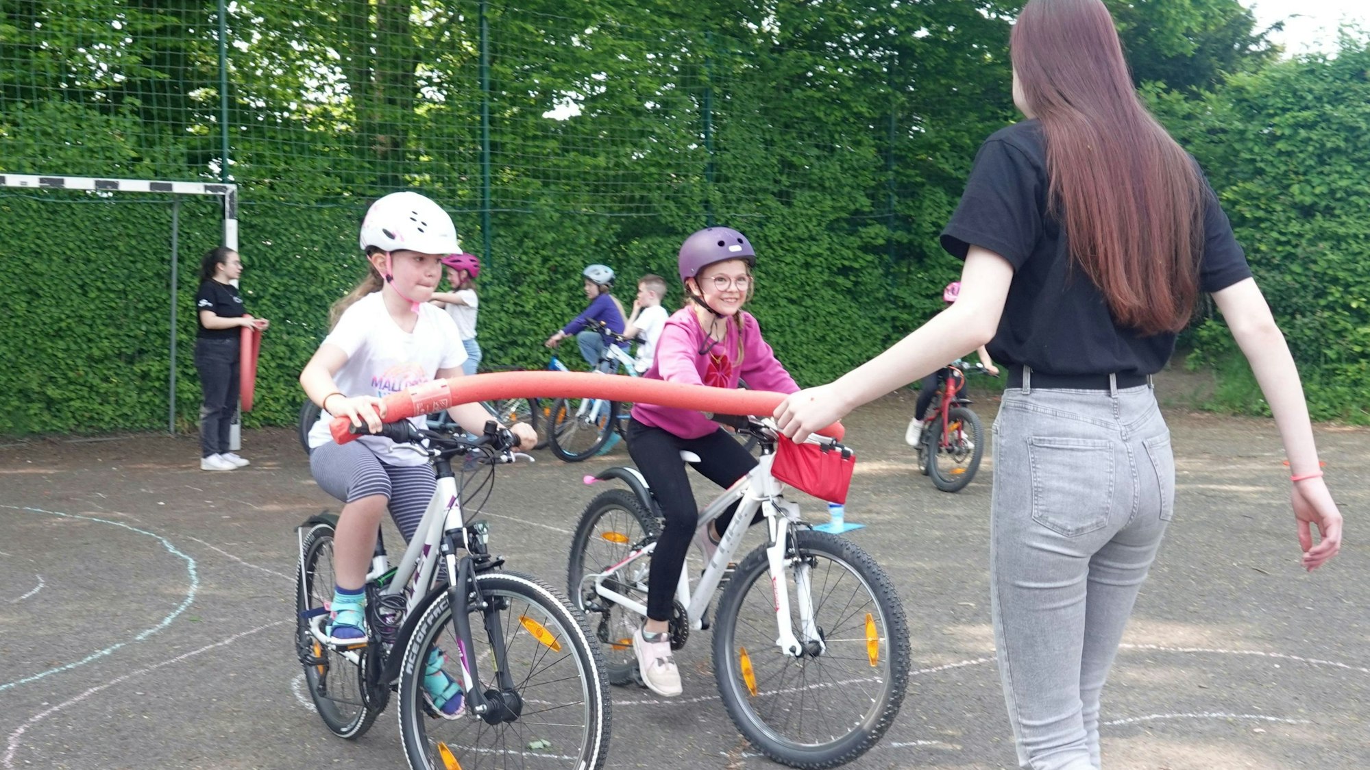 Zwei Mädchen üben unter Anleitung einer jungen Frau das Fahrradfahren.