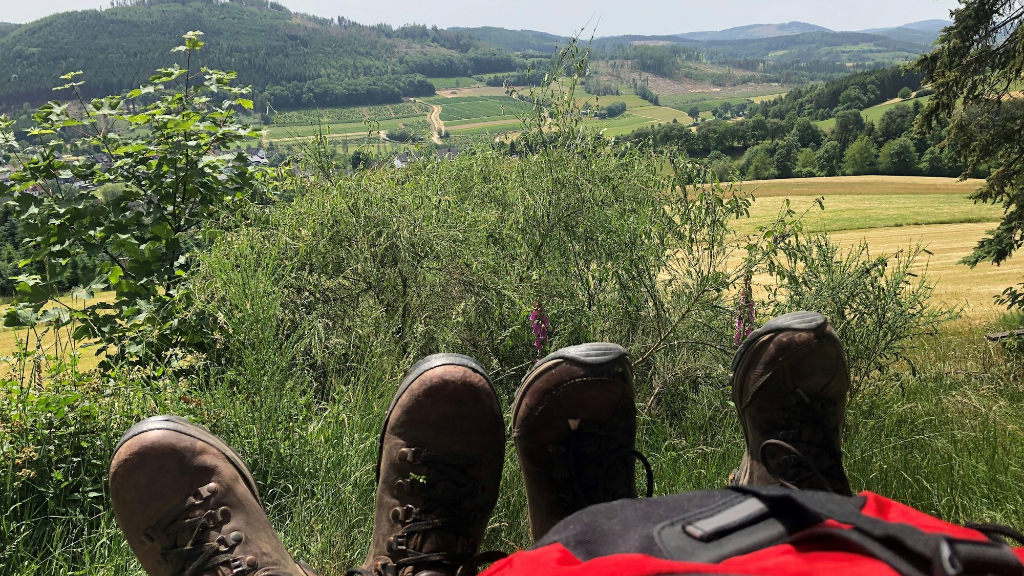 Ein Rucksack und zwei Paar Schuhe stehen vor einer Aussicht des Rothaarsteigs.