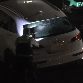 Ein Polizist steht an einem Audi mit zerschossener Heckscheibe.