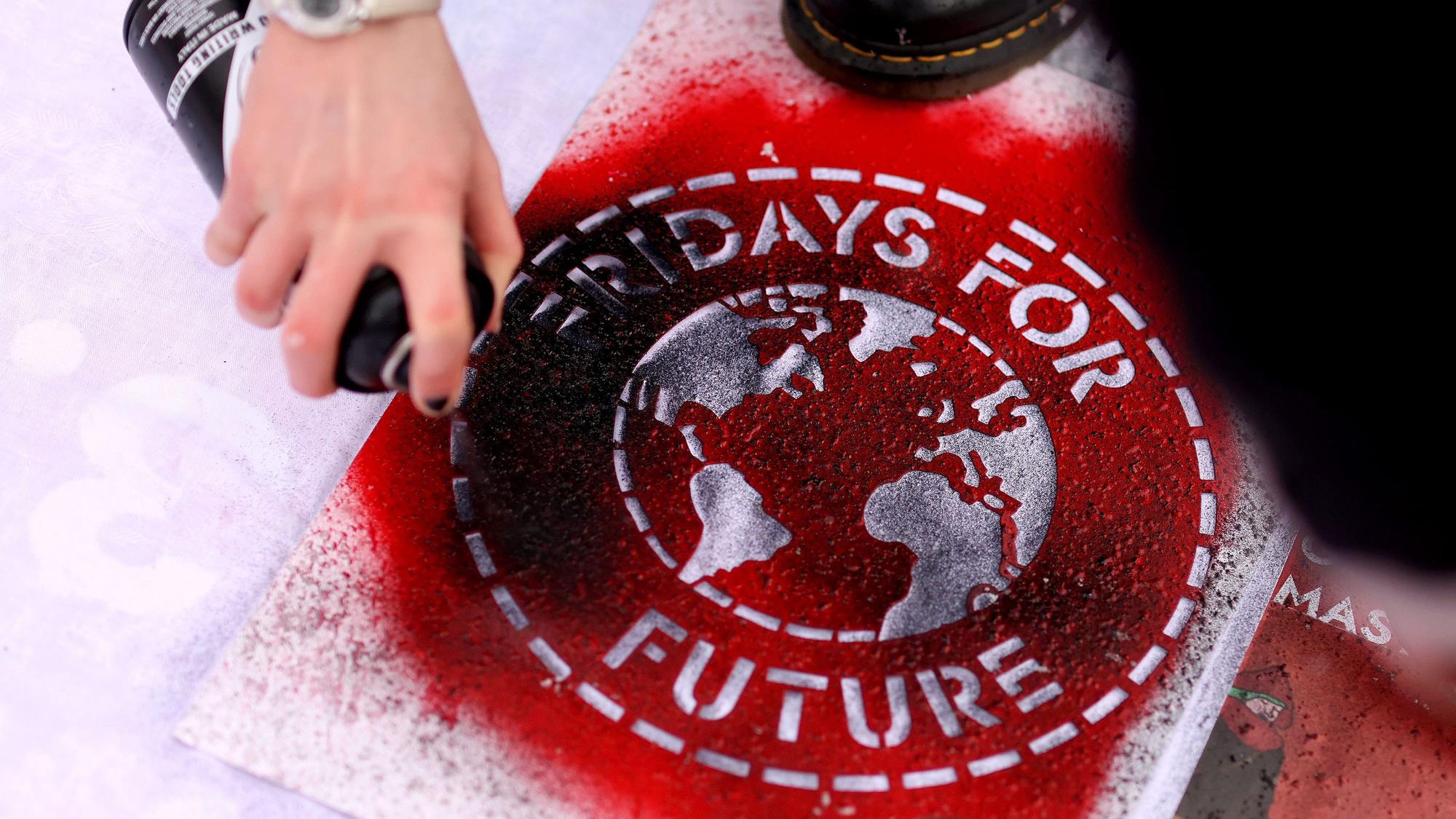 ARCHIV - 19.03.2021, Sachsen-Anhalt, Magdeburg: Eine Klimaaktivistin sprüht während einer Kundgebung ein Logo der Bewegung Fridays For Future auf ein Transparent. (zu dpa «Fridays for Future sendet 101 Klima-Fragen an die FDP») Foto: Ronny Hartmann/dpa-Zentralbild/dpa +++ dpa-Bildfunk +++