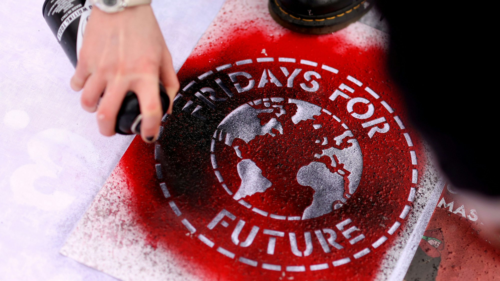 ARCHIV - 19.03.2021, Sachsen-Anhalt, Magdeburg: Eine Klimaaktivistin sprüht während einer Kundgebung ein Logo der Bewegung Fridays For Future auf ein Transparent. (zu dpa «Fridays for Future sendet 101 Klima-Fragen an die FDP») Foto: Ronny Hartmann/dpa-Zentralbild/dpa +++ dpa-Bildfunk +++