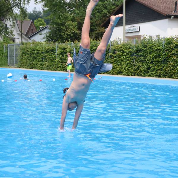 Ein Junge macht in einem Freibad einen Köpper ins Wasser.