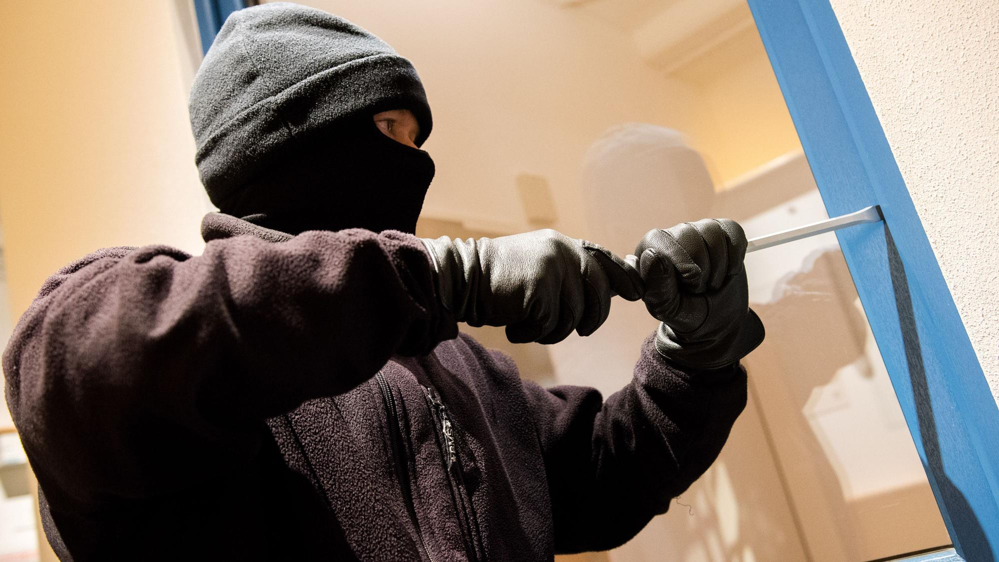 Ein als Einbrecher verkleideter Mann hebelt in der Kriminalpolizeilichen Beratungsstelle der Polizei ein Fenster auf.