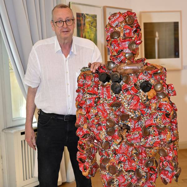 Dirk Kästel steht neben einem Kunstwerk, das HA Schult für die Ausstellung gespendet hat.
