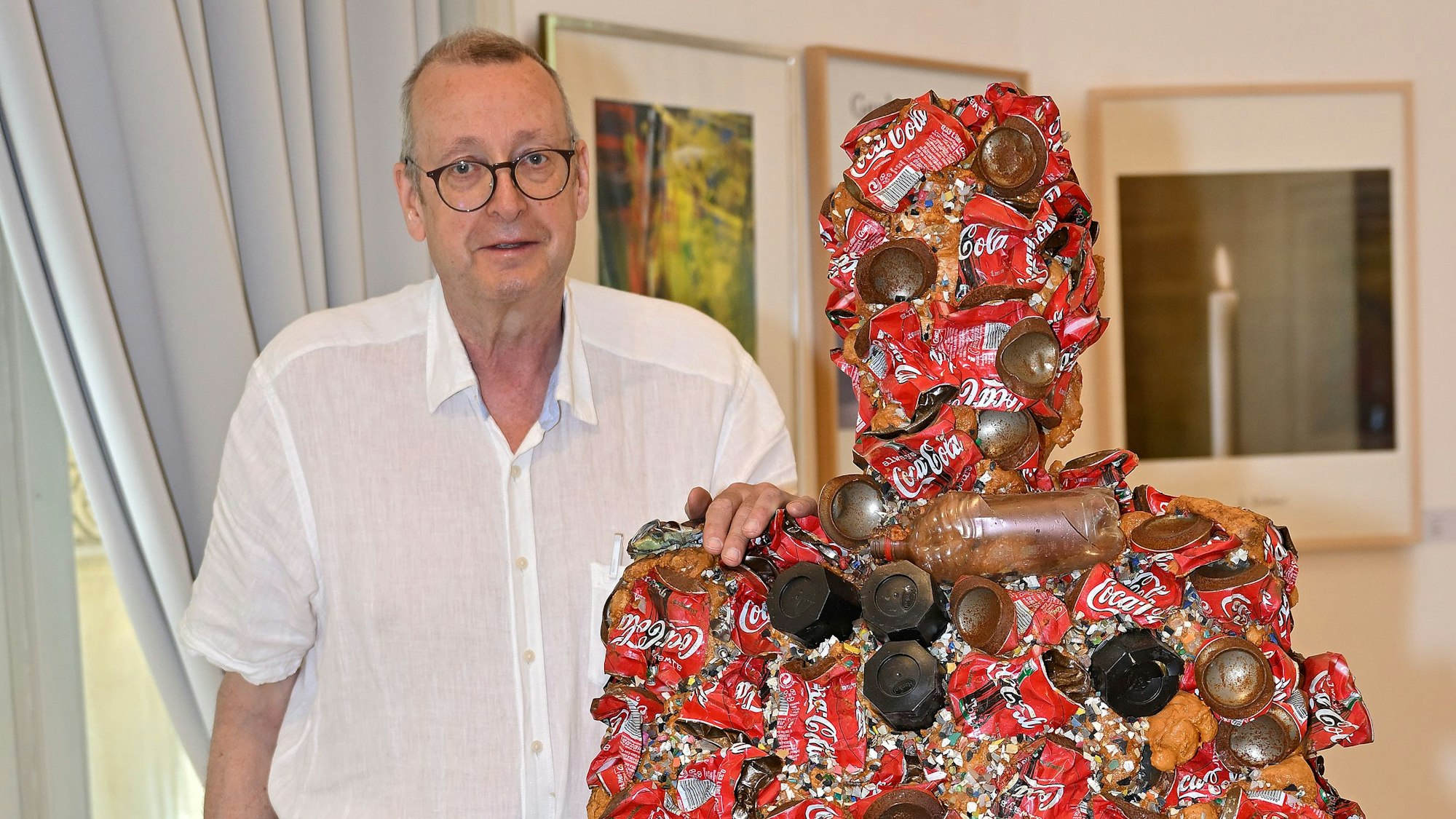 Dirk Kästel steht neben einem Kunstwerk, das HA Schult für die Ausstellung gespendet hat.