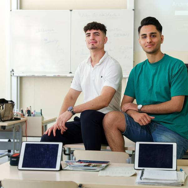Zwei junge Männer sitzen in einer Schulklasse des Berufskollegs Südstadt auf einem Pult.