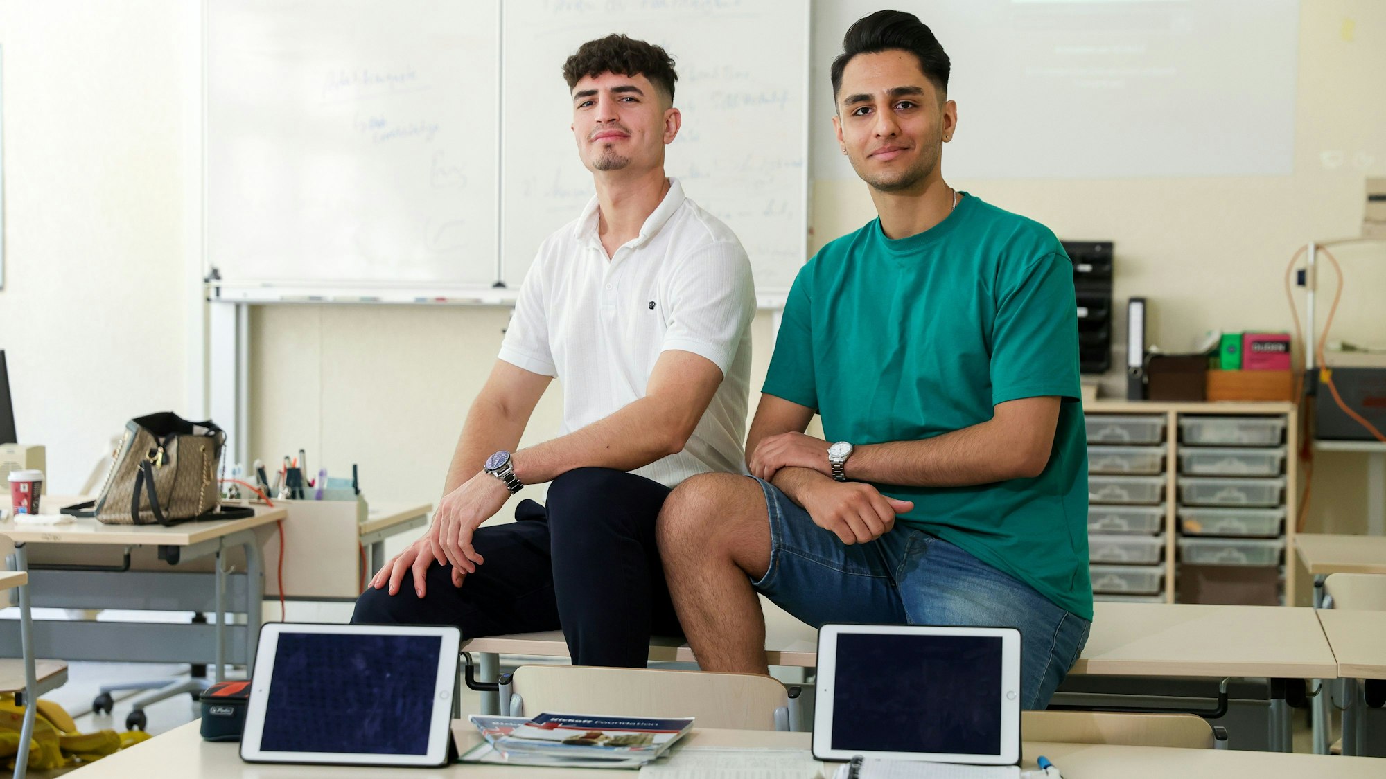 Zwei junge Männer sitzen in einer Schulklasse des Berufskollegs Südstadt auf einem Pult.