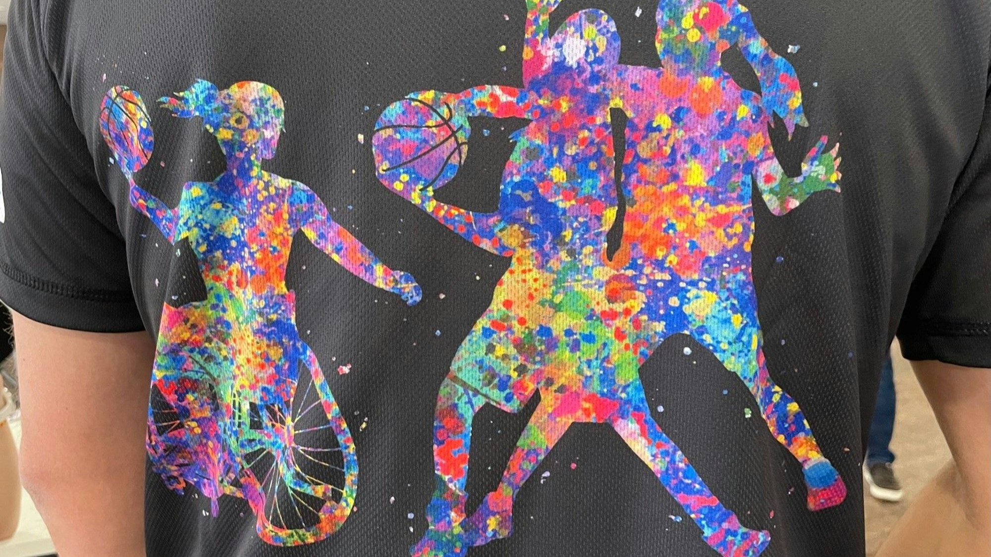 Auf den T-Shirts für die inklusive Sportwoche sind Kinder zu sehen, die Rollstuhlbasketball spielen.