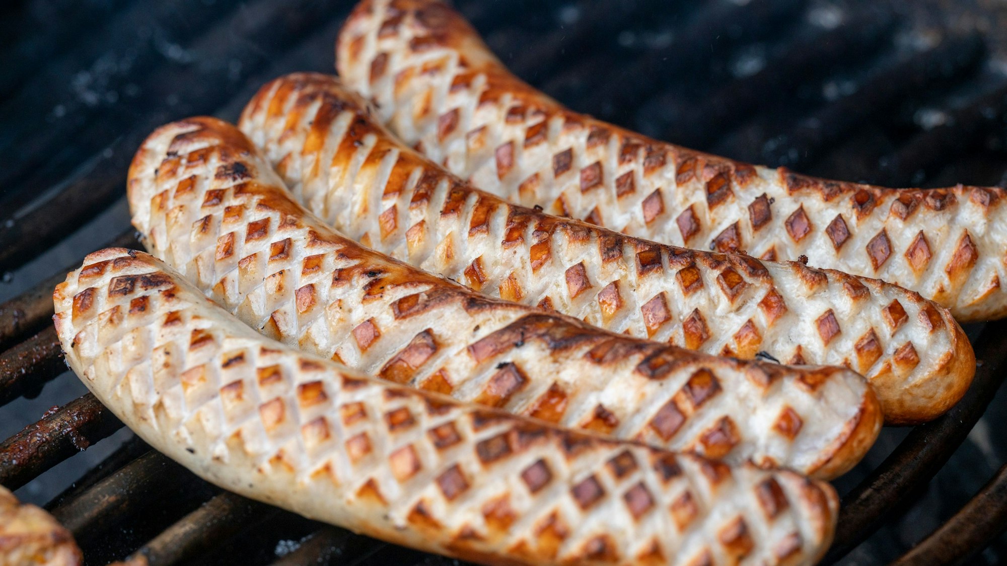 Im Zickzack eingeritzte gegrillte Würstchen liegen auf einem Grill.