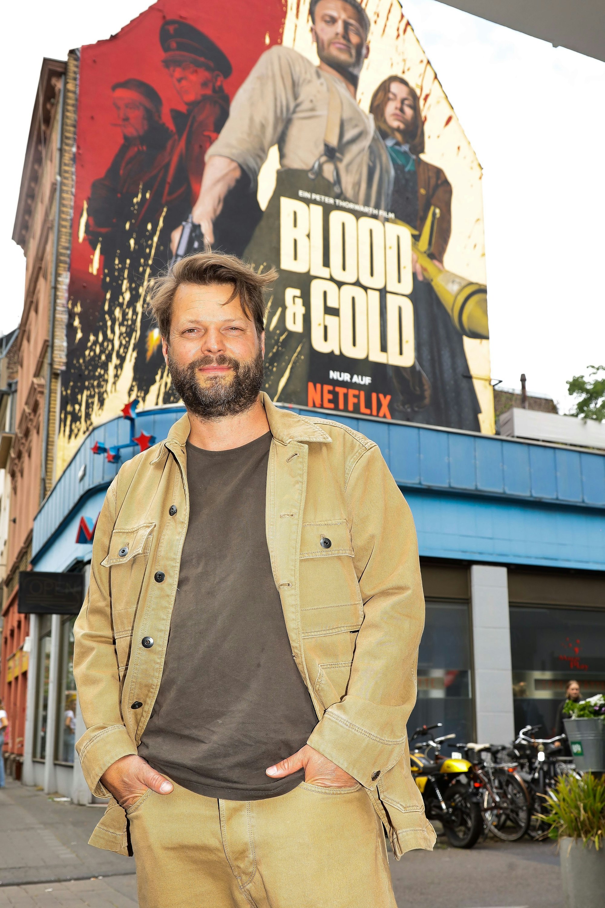 Regisseur Peter Thorwarth auf der Venloer Straße, Ecke Körnerstraße vor der riesigen Werbung für den Netflix-Film „ Blood & Gold“