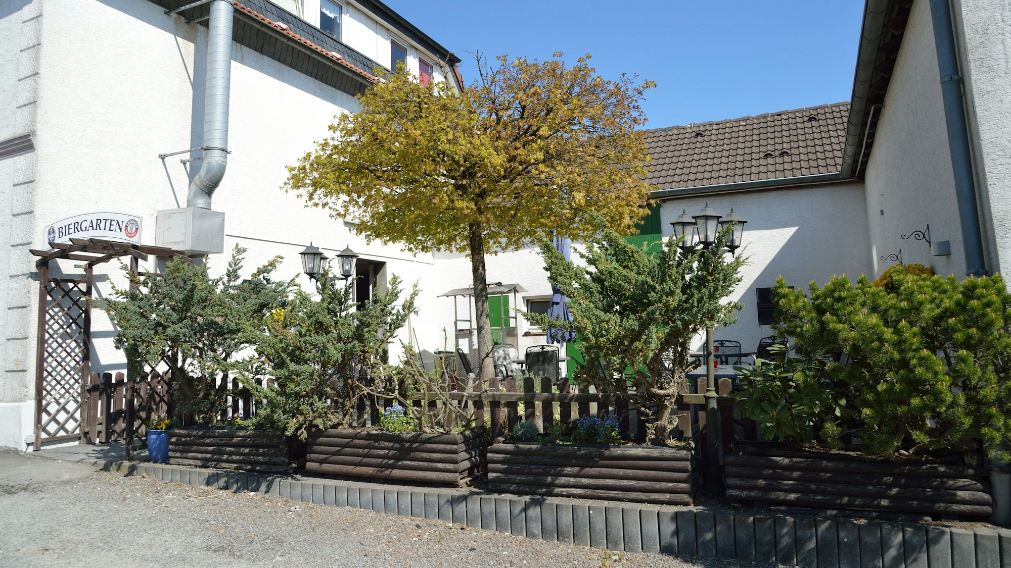 Hinter Bäumen und Sträuchern ist ein Biergarten.