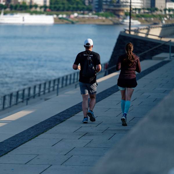 Zwei Jogger laufen in der frischen Morgenluft auf der Rheinpromenade am Rhein entlang.