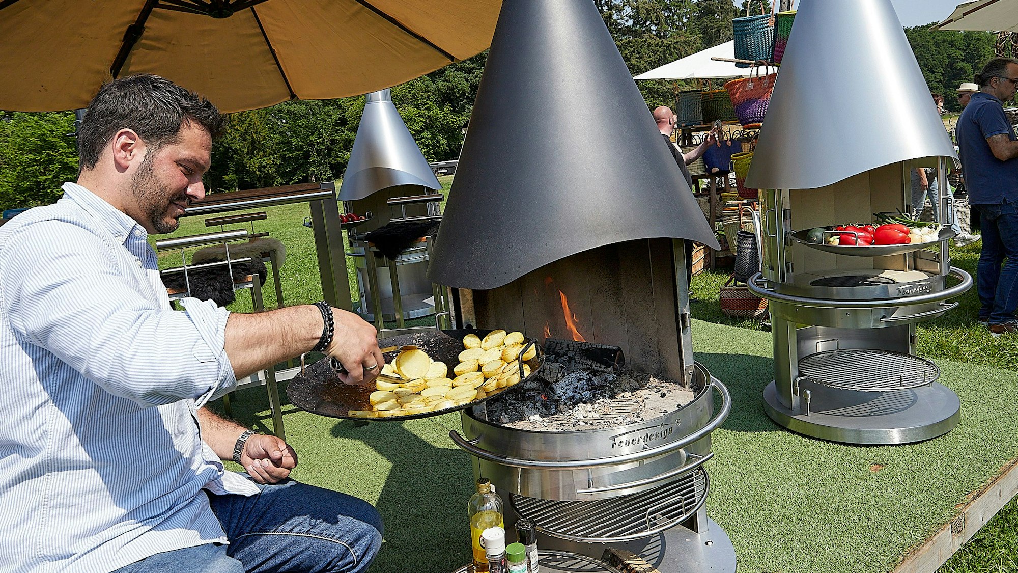 Das Bild zeigt einen Mann, der einen Grillkamin mit Kartoffelscheiben bestückt, um diese zu garen.