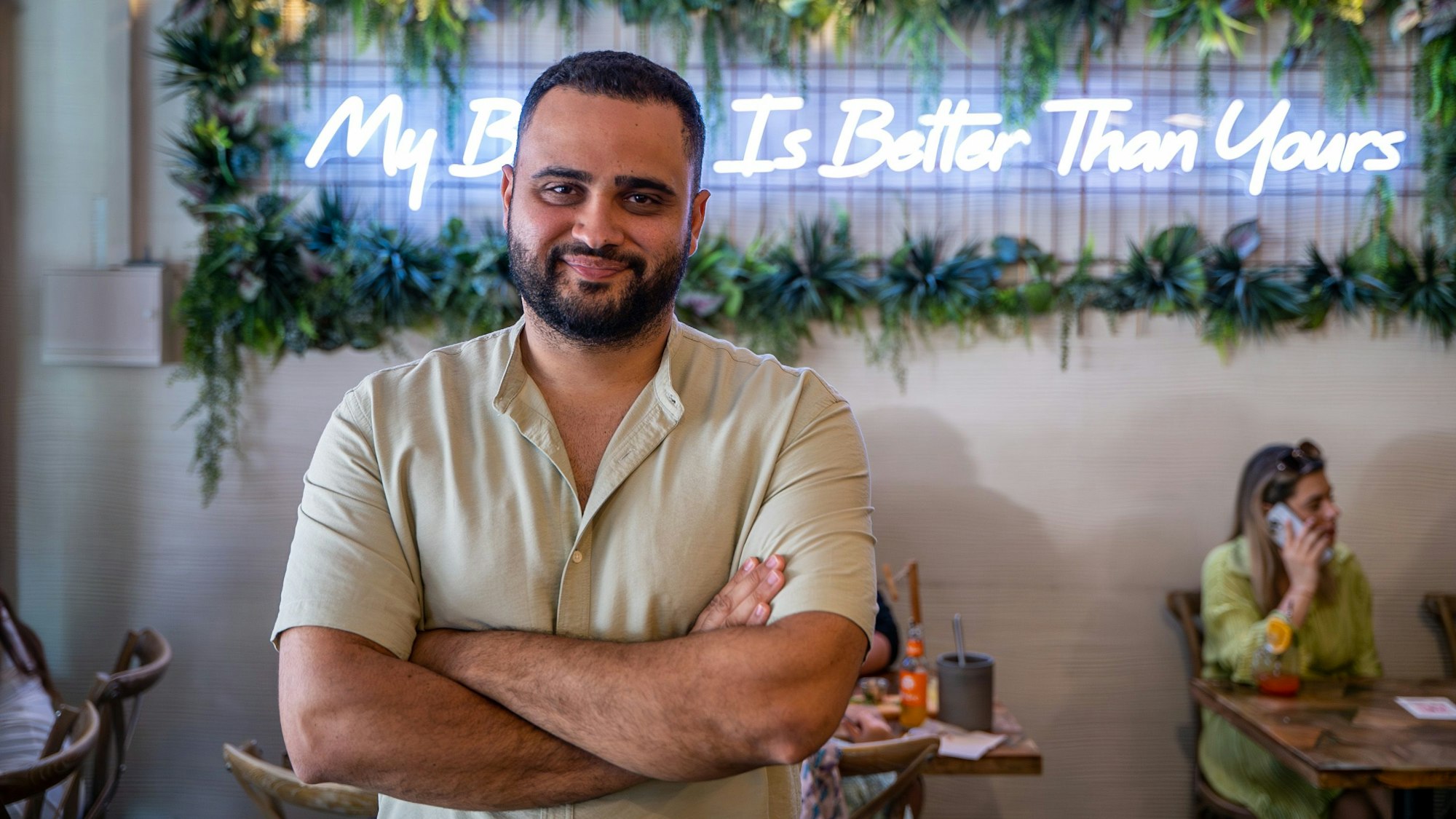 Parham Pooramin im Café Buur vor einem leuchtenden Schriftzug: „My Brunch Is Better Than Yours.“