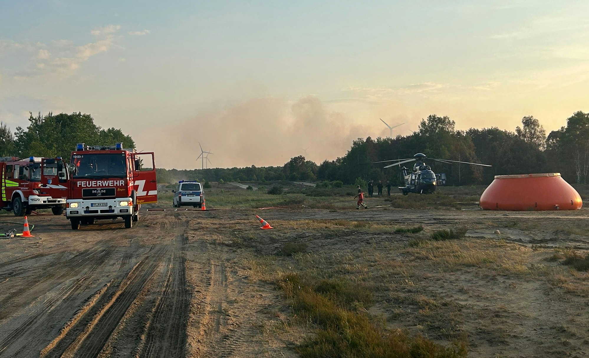 Feuerwehrkräfte sind neben einem Löschhubschrauber in einem Waldstück nahe Jüterbog im Einsatz.