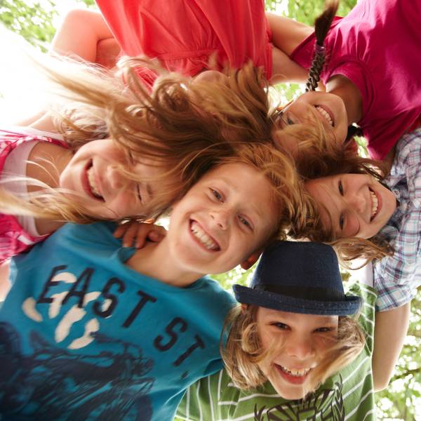 Fünf lachende Kinder stehen im Kreis und stecken ihre Köpfe aneinander.