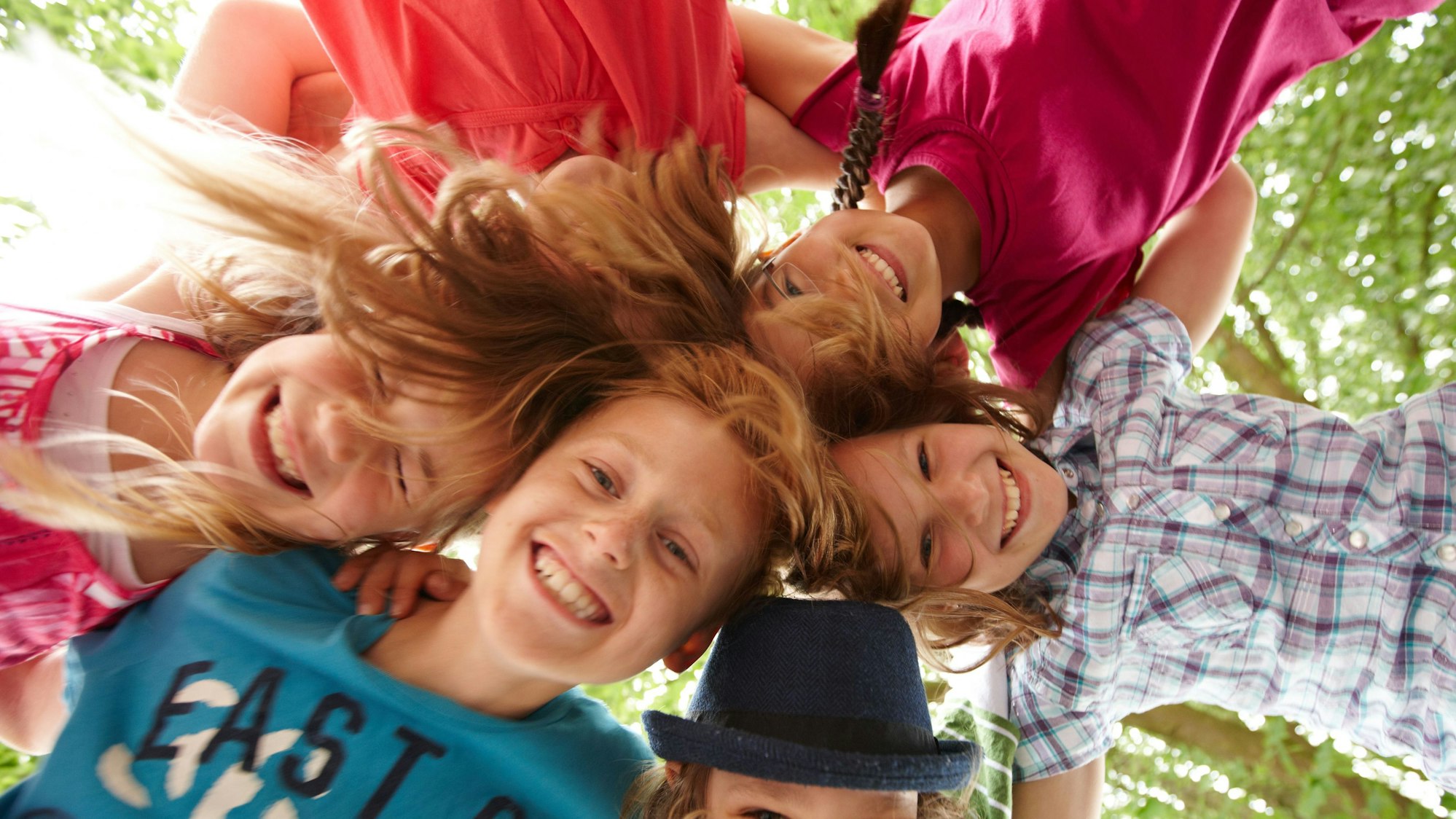 Fünf lachende Kinder stehen im Kreis und stecken ihre Köpfe aneinander.