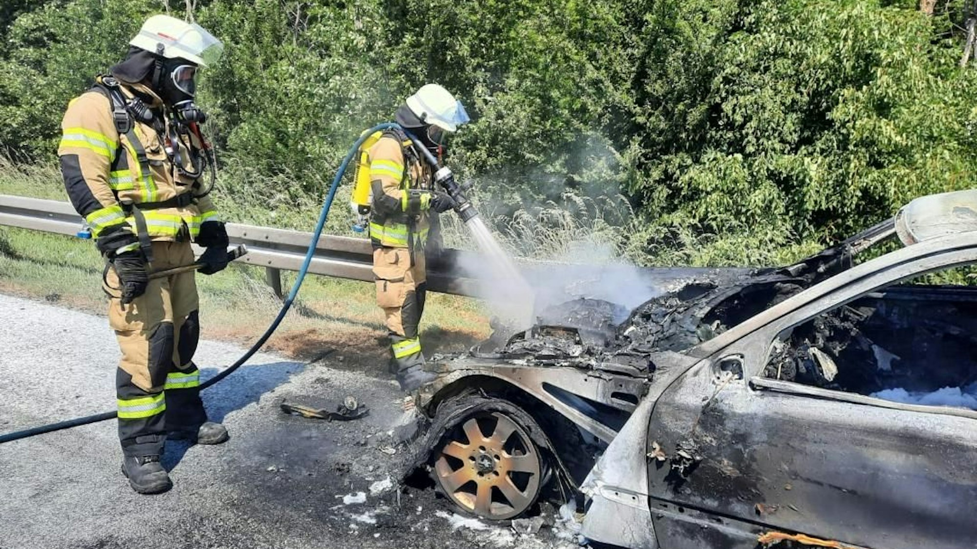 Feuerwehrleute löschen ein brennendes Auto.