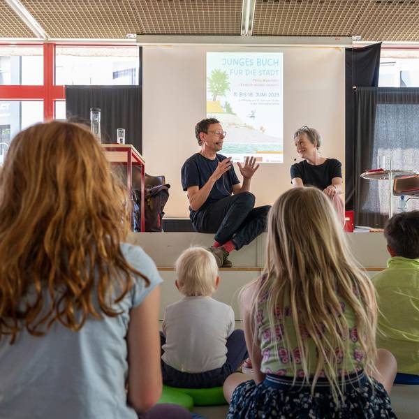 Philip Waechter sitzt mit Moderatorin Britta Weyers auf einer Bühne, davor sitzen Kinder.