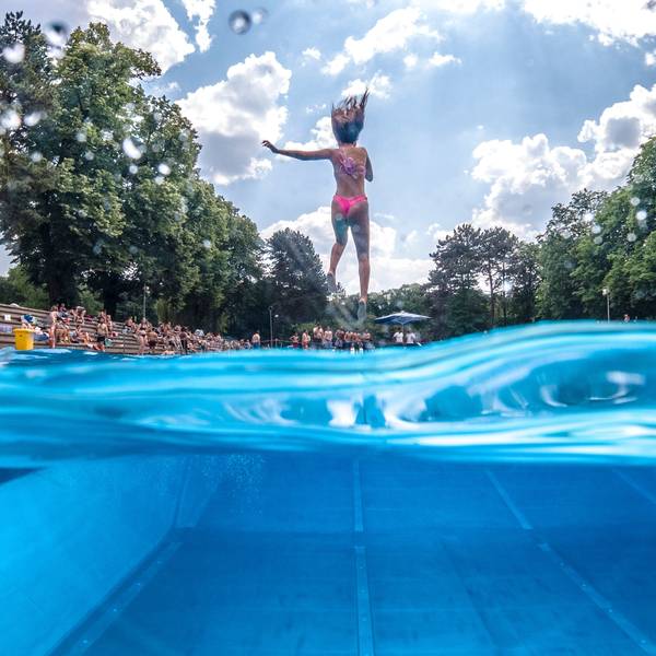 Der Sprung ins kalte Wasser des Stadionbads ist im Kölner Großstadtsommer eine beliebte Abkühlung: Eine Frau springt mit zugehaltener Nase in ein Freibadbecken.