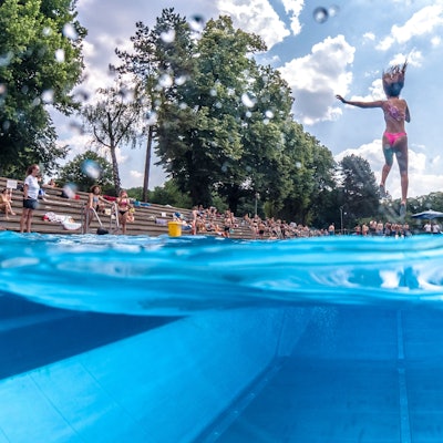 Der Sprung ins kalte Wasser des Stadionbads ist im Kölner Großstadtsommer eine beliebte Abkühlung: Eine Frau springt mit zugehaltener Nase in ein Freibadbecken.