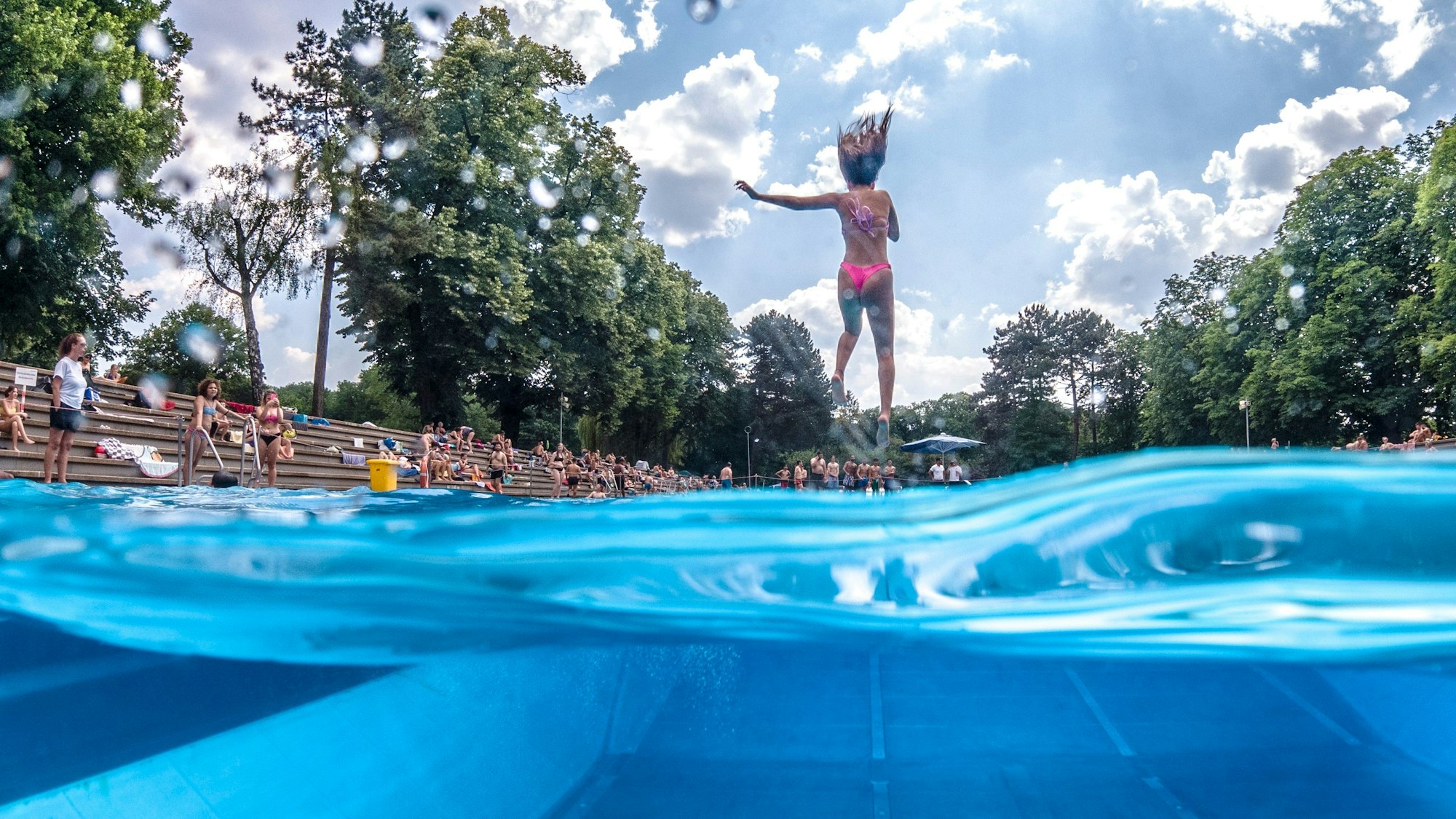 Der Sprung ins kalte Wasser des Stadionbads ist im Kölner Großstadtsommer eine beliebte Abkühlung: Eine Frau springt mit zugehaltener Nase in ein Freibadbecken.