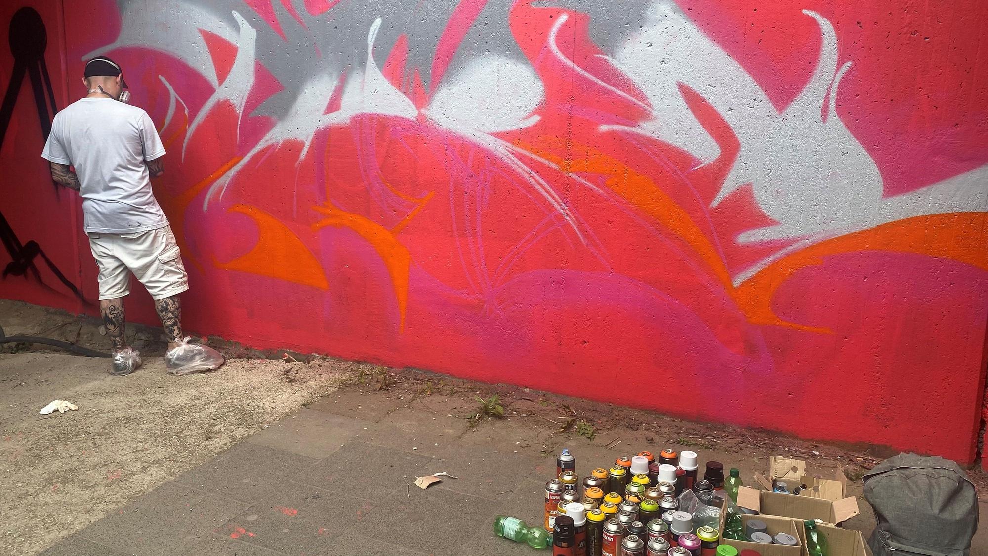 Sprayer One Take vor einer Graffiti-Wand.