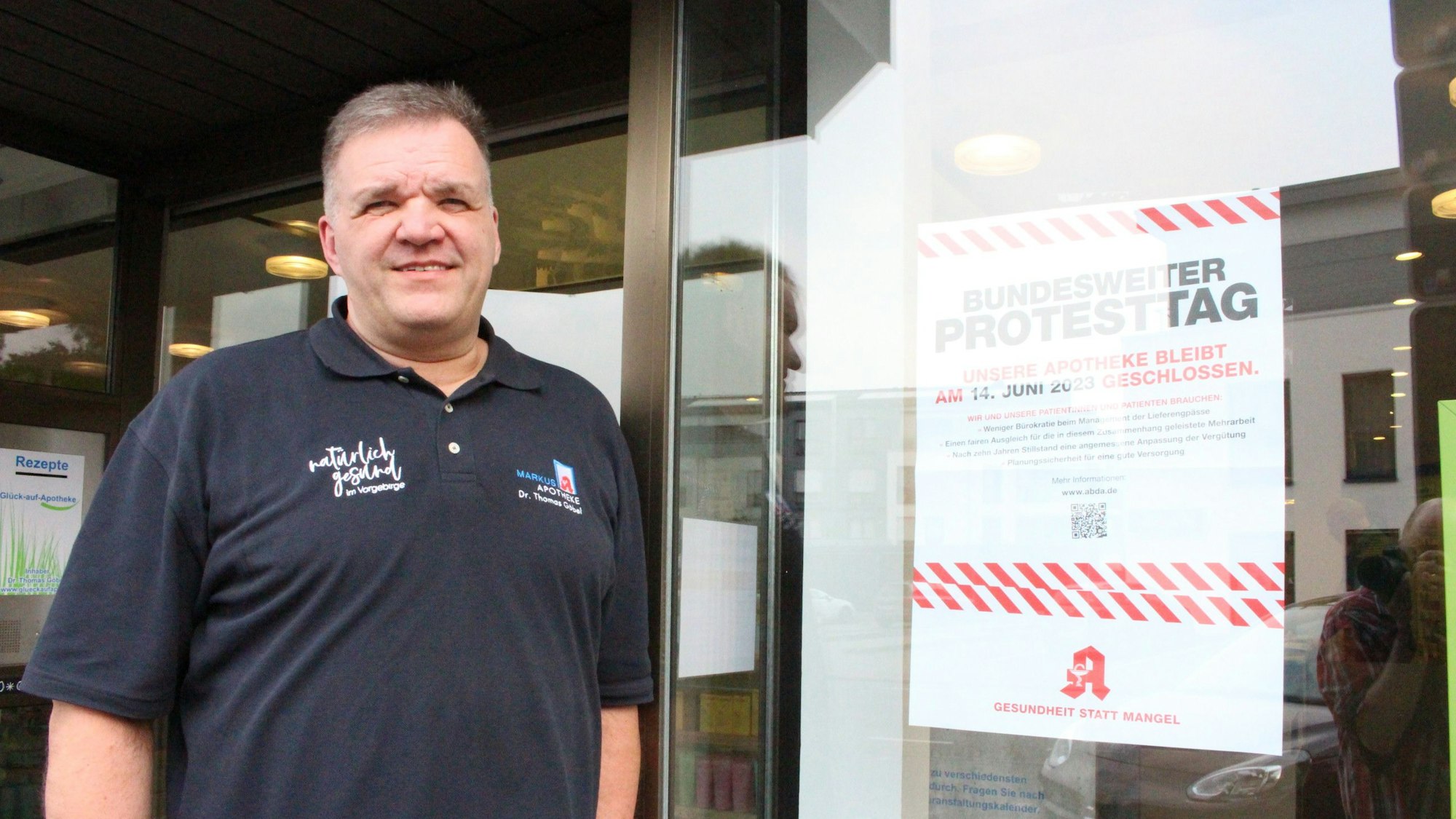 Das Bild zeigt Dr. Thomas Göbel vor seiner Apotheke in Mechernich. An der Tür hängt ein Plakat, das auf den Protesttag hinweist.
