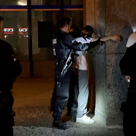 Ein Mann steht an einer Wand und wird von Polizeikräften abgetastet.
