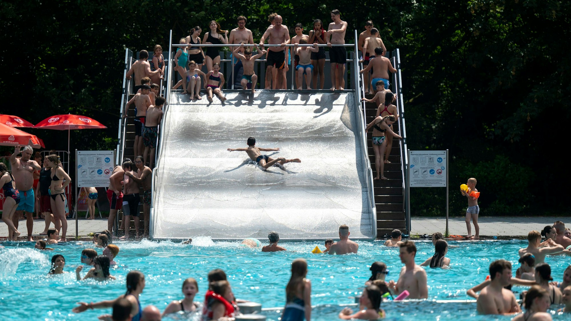 Menschen sind im Stadionbad in einem Becken zu sehen. Auf einer Rutsche stehen viele Menschen an.