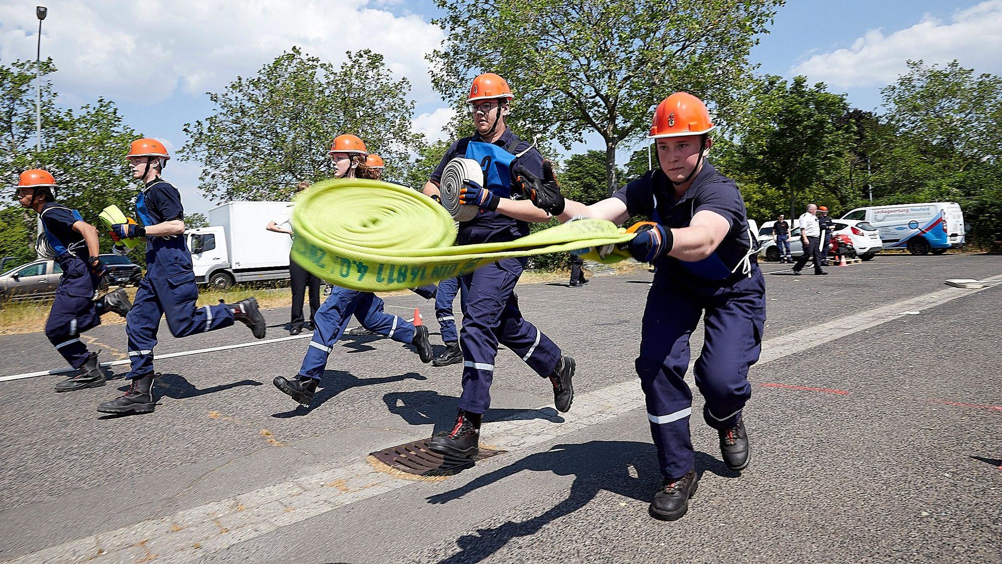 Einige Jugendfeuerwehrleute laufen mit Schläuchen über einen Platz, einer wirft den Schlauch aus.