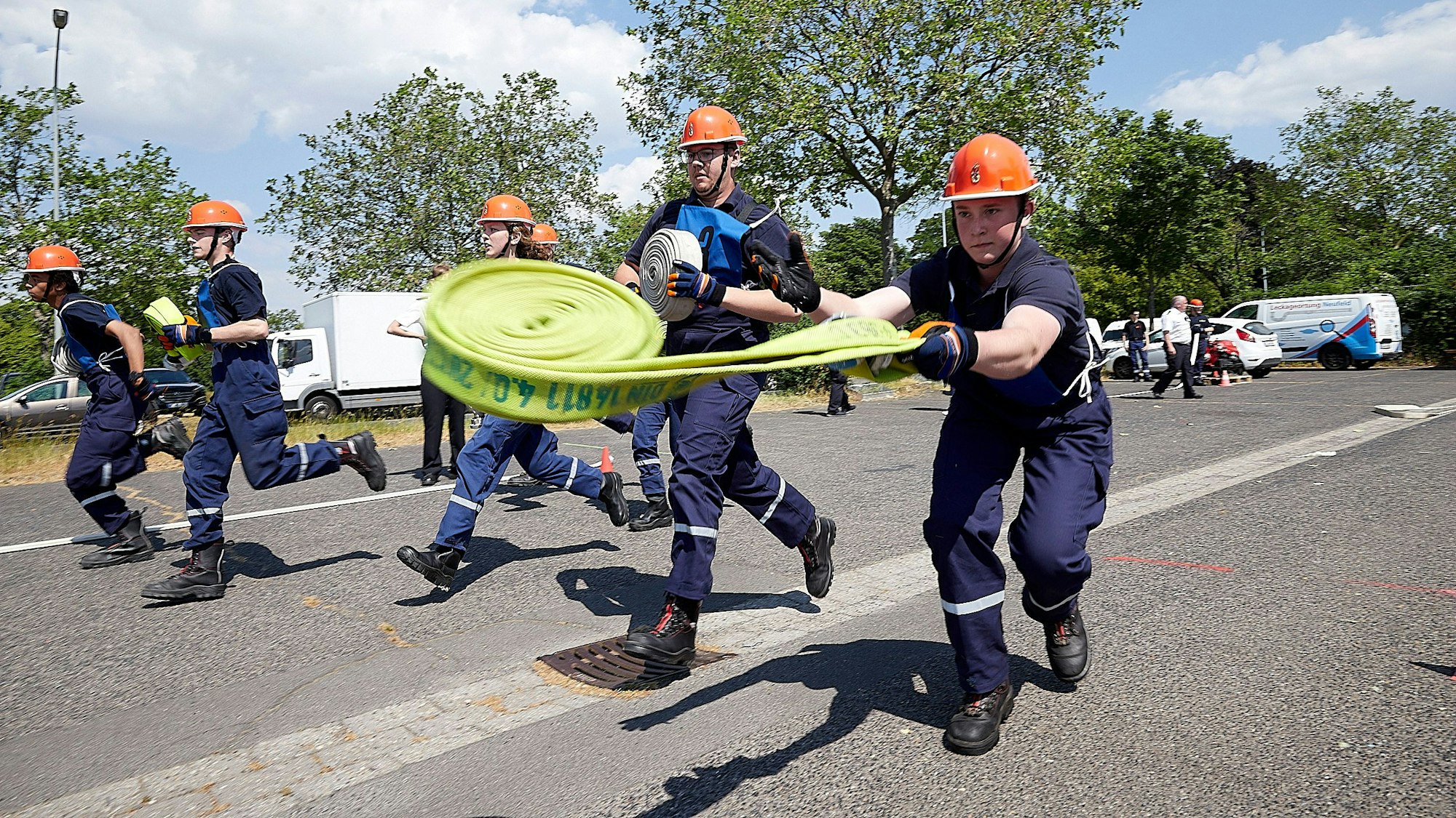 Einige Jugendfeuerwehrleute laufen mit Schläuchen über einen Platz, einer wirft den Schlauch aus.