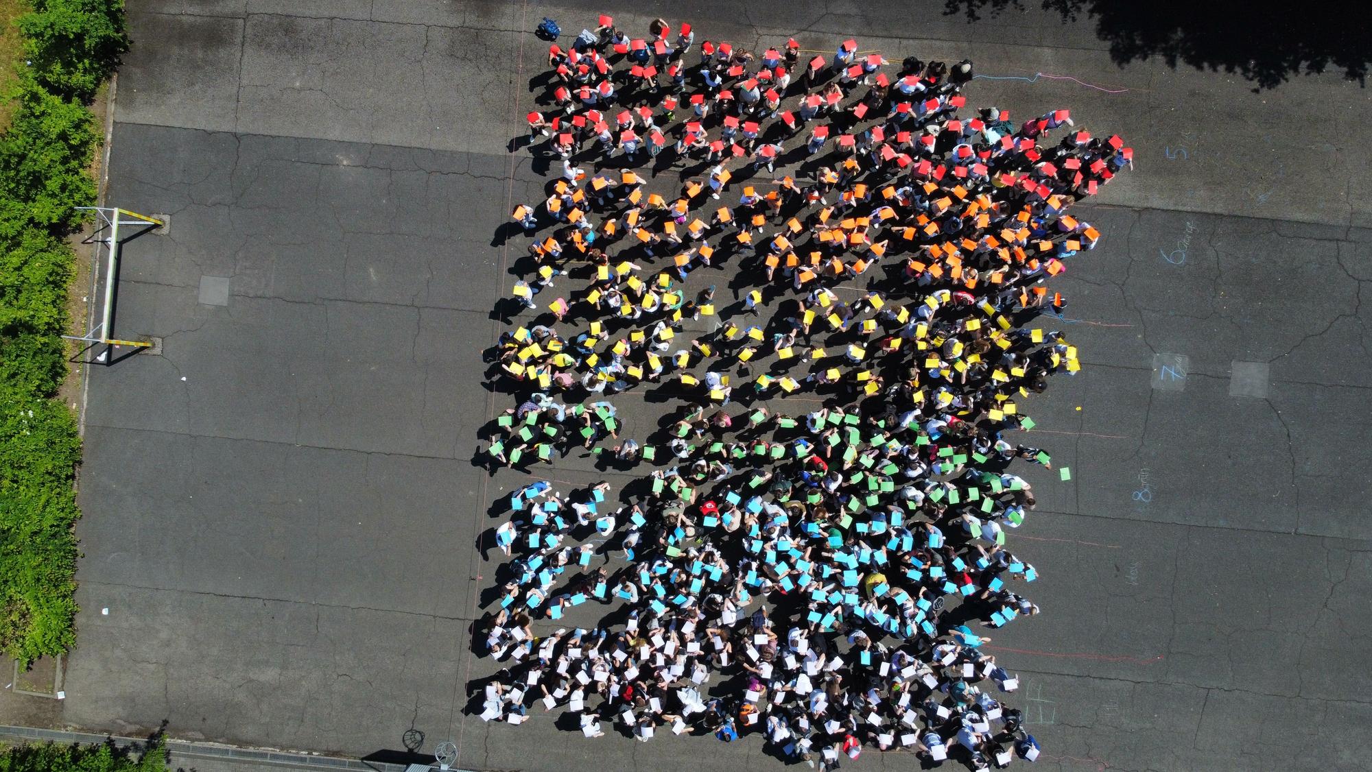 Schüler halten bunte Plakate hoch und stellen die Regenbogenflagge nach.