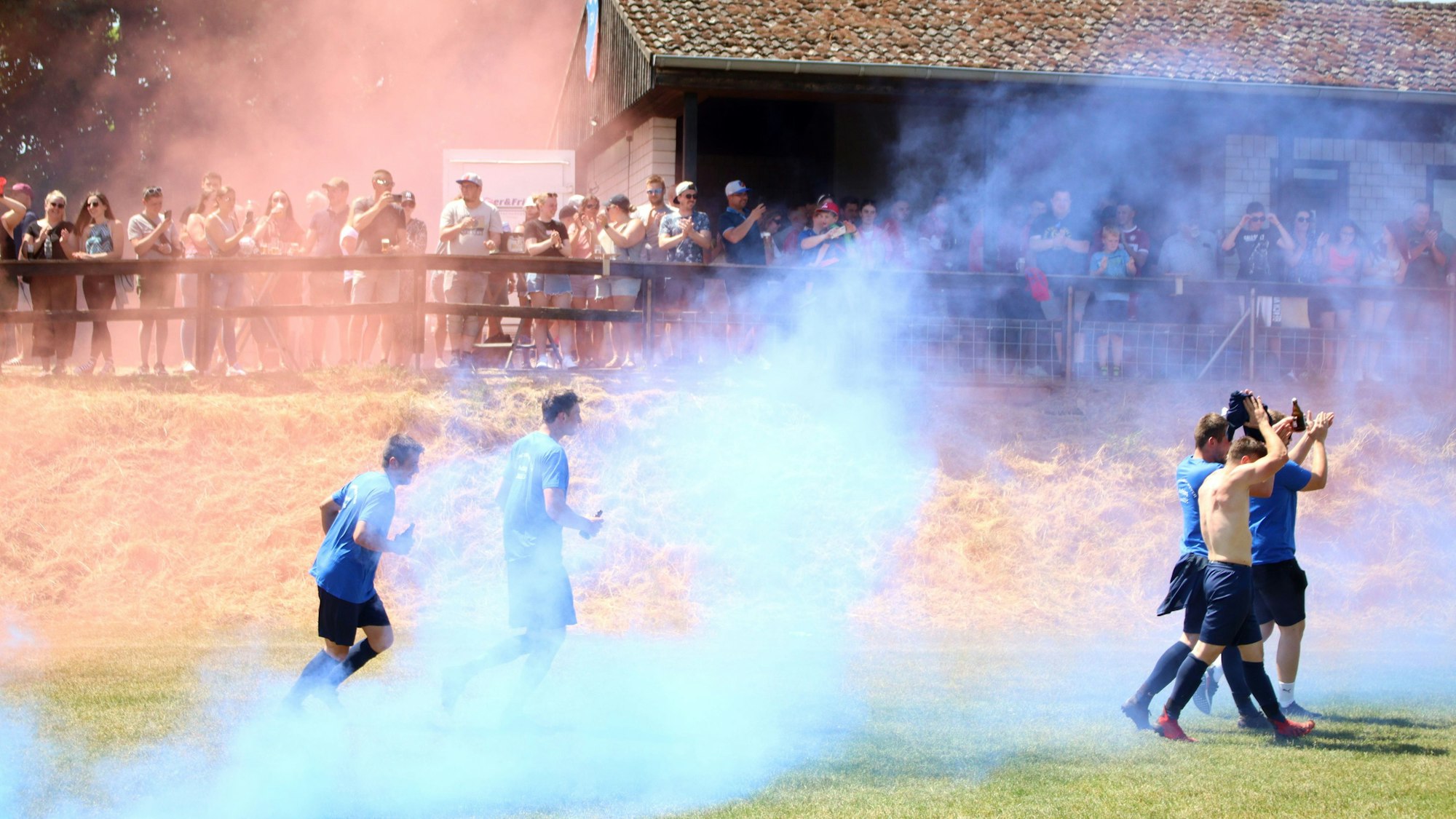 Fußballspieler von Concordia Weyer applaudieren den Fans. Rot-blauer Nebel verhüllt sie.