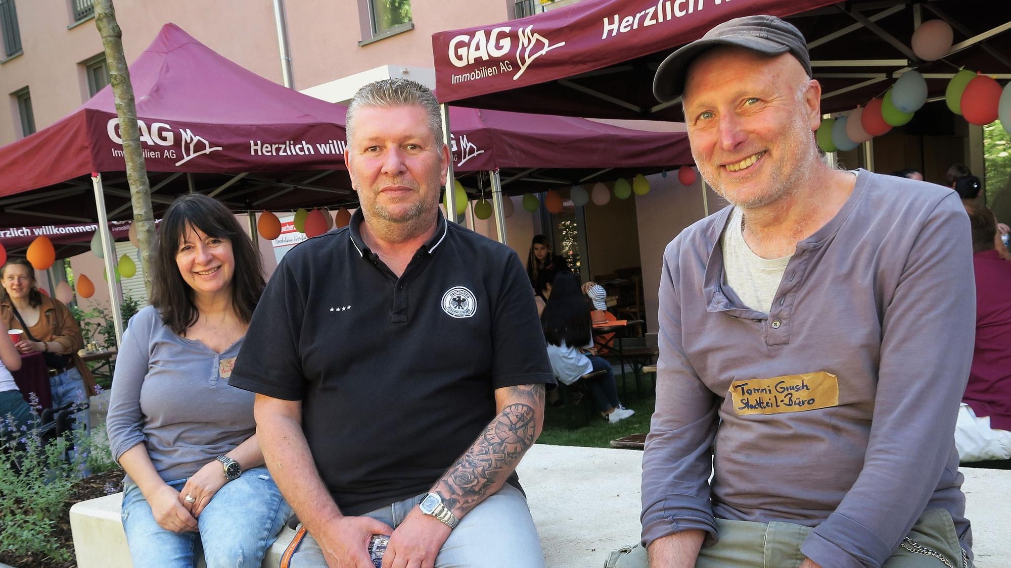 Eine Frau und zwei Männer sitzen vor einem Stand der GAG.