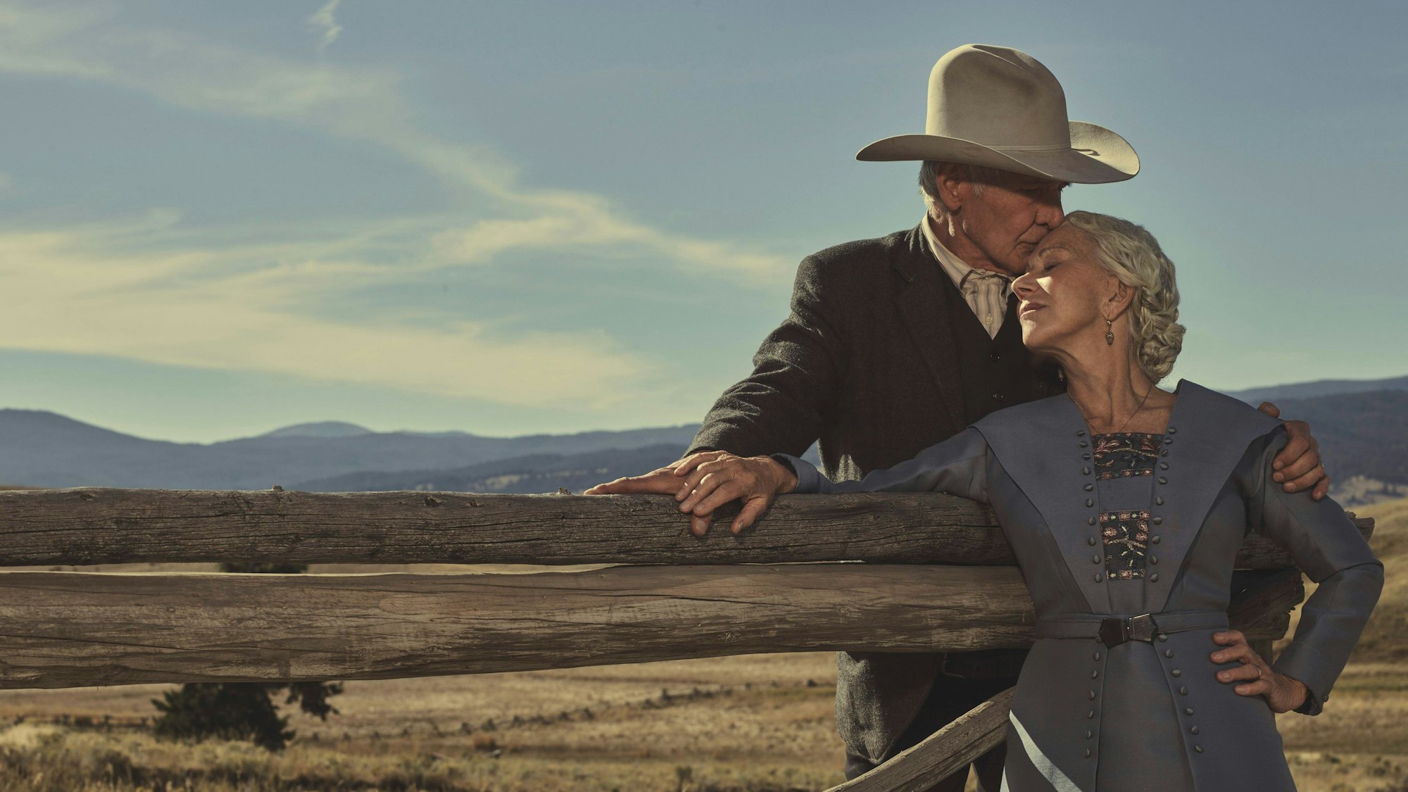 Harrison Ford und Helen Mirren sind gehoben im Stil der 20er gekleidet, Ford trägt einen Cowboy-Hut. Sie lehnen zusammen an einem Holzzaun, im Hintergrund die Landschaft von Montana.