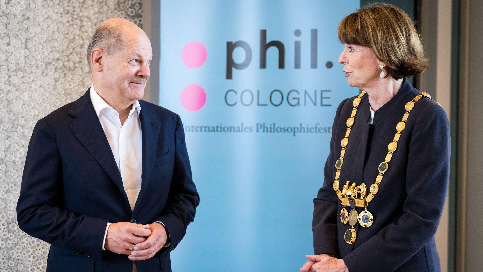 Kanzler Scholz und OB Reker (r.) vor einem Plakat des Philosophie-Festivals „Phil-Cologne“