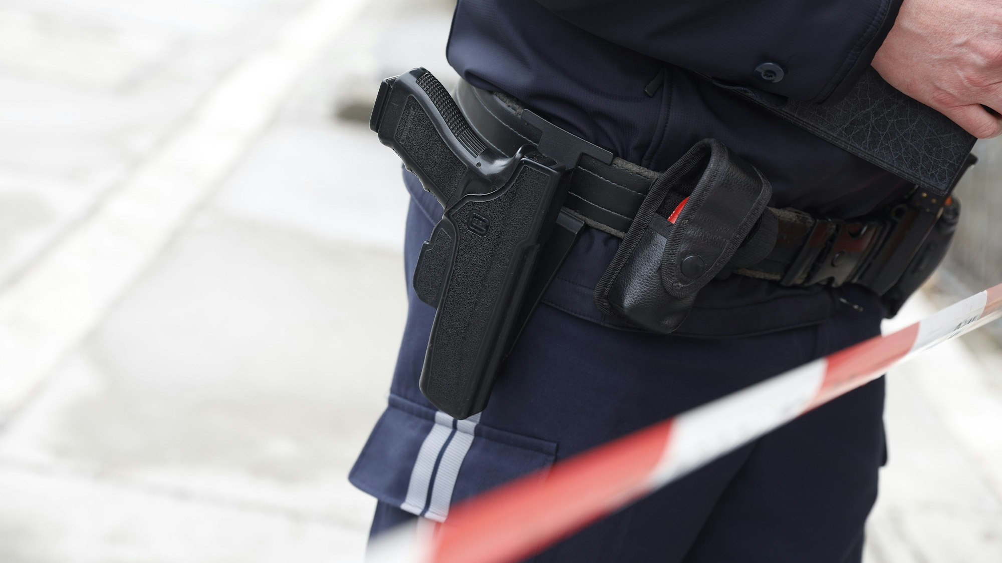 Ein Polizist steht mit einer Pistole auf der Straße. Man sieht Absperrband.