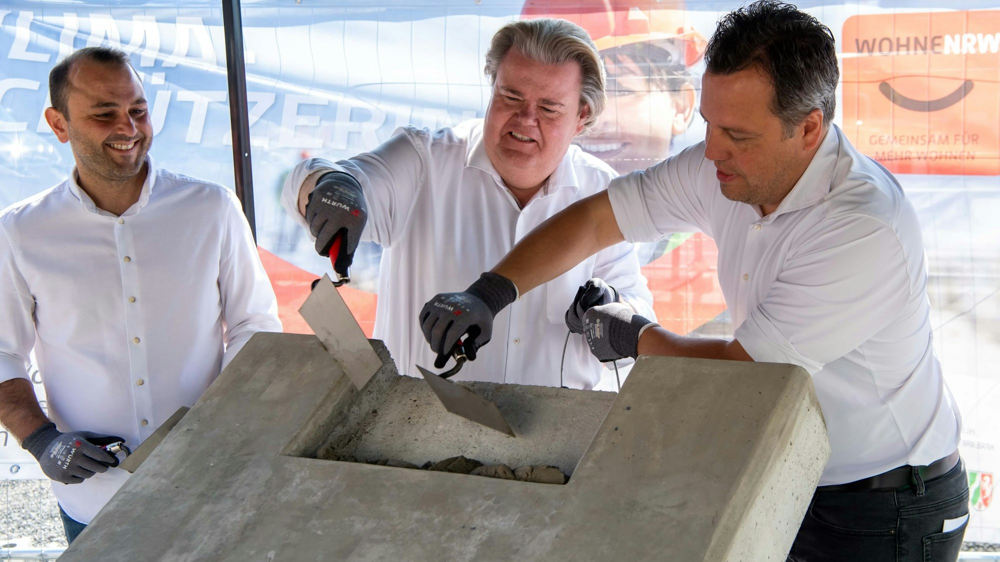 Das Foto zeigt Architekt Adam Fray (v.l.), Klaus Voussem (NRW-Bank-Vertreter) und Bürgermeister Sacha Reichelt bei der Grundsteinlegung für das Mehrfamilienhaus an der Wilhelmstraße.