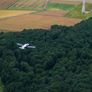 Auf unserem Symbolfoto ist ein Kleinflugzeug über einem Waldstück zu sehen.