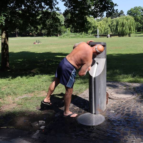 Ein Mann trinkt im Park aus einem Trinkwasserspender.