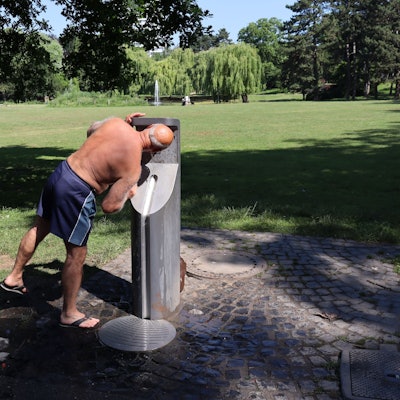 Ein Mann trinkt im Park aus einem Trinkwasserspender.