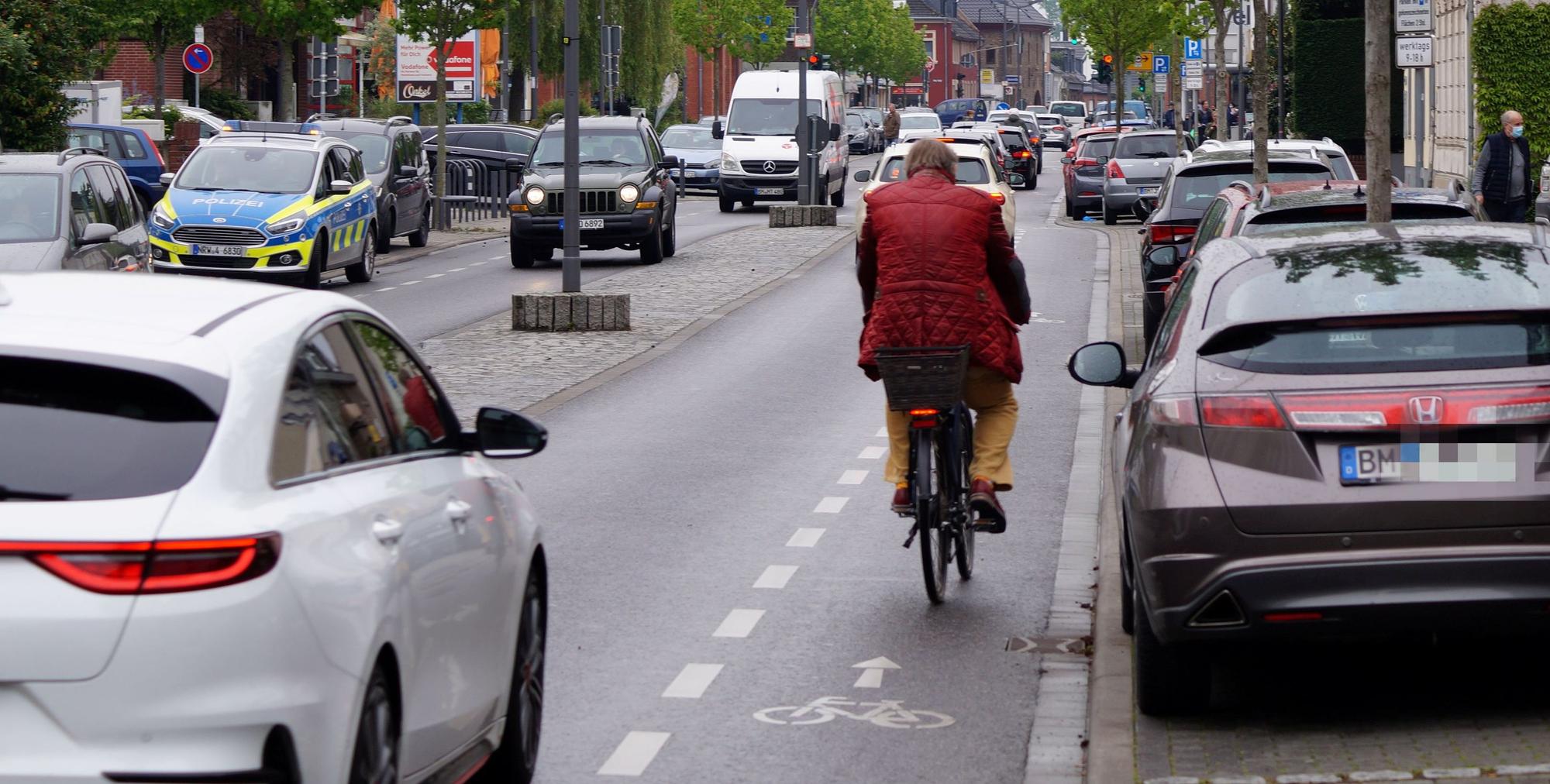 Das Foto zeigt einen Fahrradfahrer auf der Hahnenstraße in Kerpen: rechts geparkte Autos, links fahren Autos in geringem Abstand an ihm vorbei.