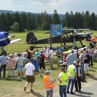 Zahlreiche Leute schauen sich auf einer großen Wiese ein Kleinflugzeug an.