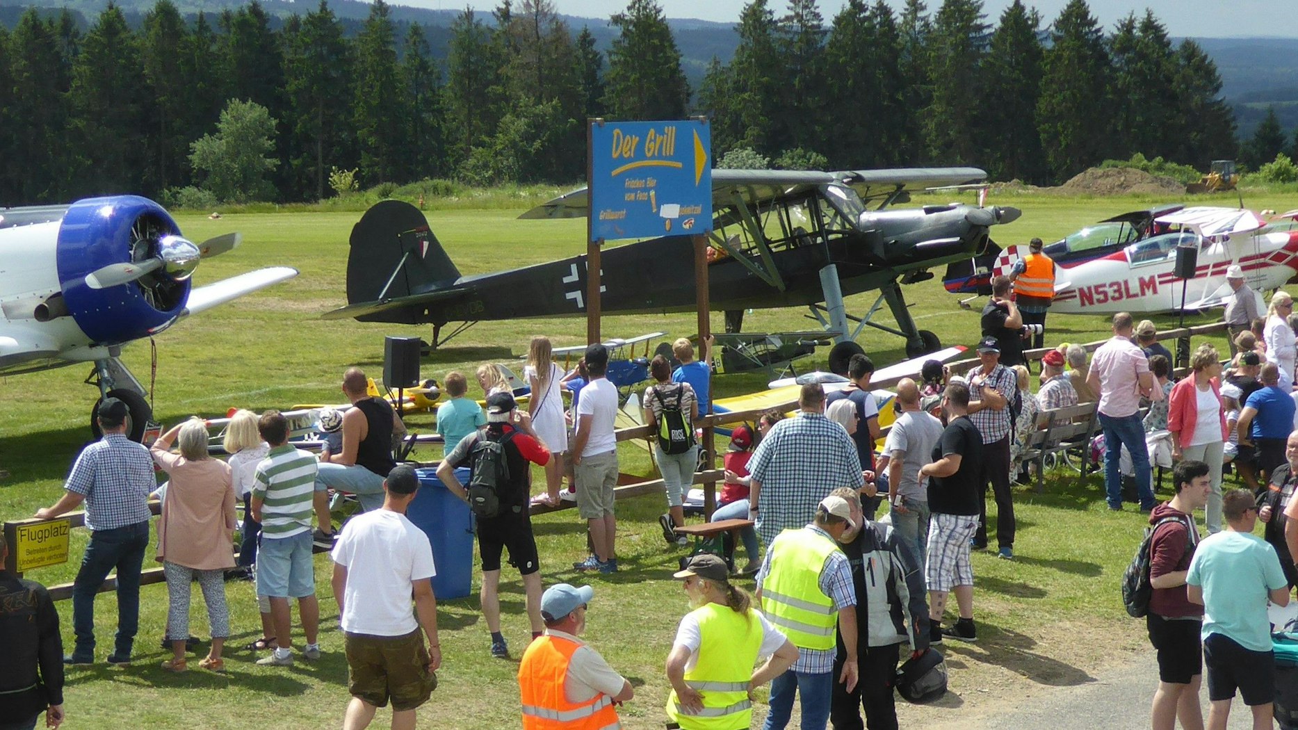 Zahlreiche Leute schauen sich auf einer großen Wiese ein Kleinflugzeug an.