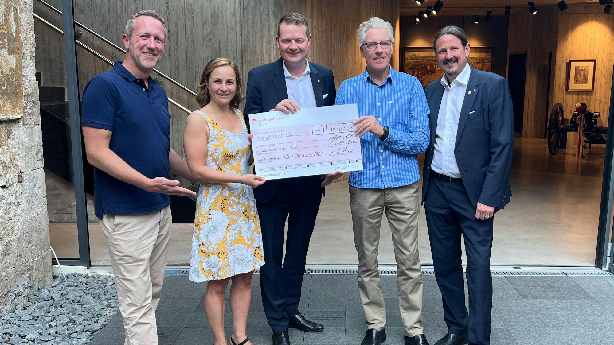 Die Beteiligten halten einen großen Spenden-Scheck.