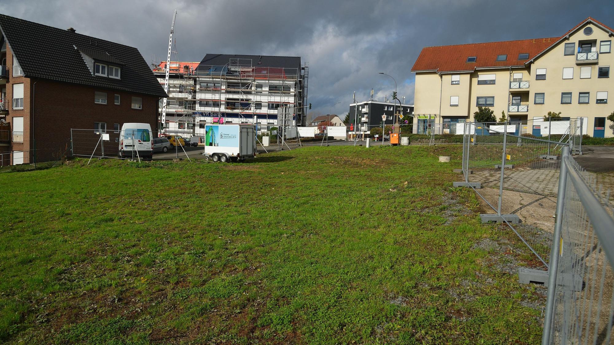 Rechts am Bildrand sind die Absperrgitter um eine grüne Wiese zu sehen. Im Hintergrund sowie am linken Bildrand sind Wohnhäuser zu sehen.
