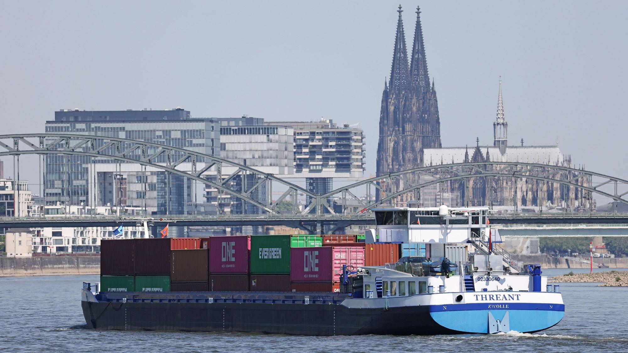 Ein Binnenschiff, mit Containern beladen, fährt in Köln vor dem Dom und den Kranhäusern über den Rhein.