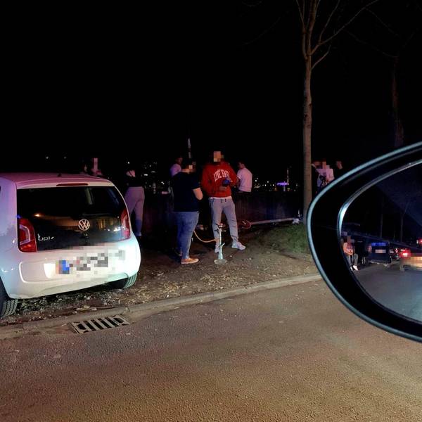 Junge Männer stehen um geparkte Autos auf der Alfred-Schütte-Allee herum und rauchen Shisha.